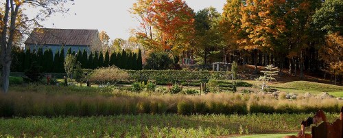 A scenic landscape featuring a garden, trees with autumn foliage, and a rustic building in the background.