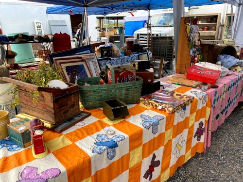 A vibrant outdoor market table covered with colorful quilts, vintage items, and various collectibles for sale.