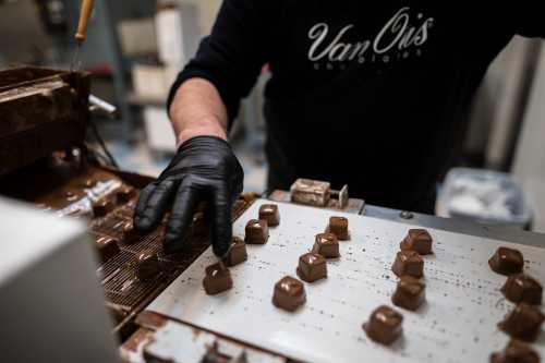 A person in a black glove works with chocolate molds in a confectionery setting.