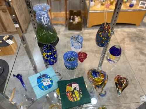 A display of colorful glass art pieces, including vases, bowls, and decorative items, on a glass table.