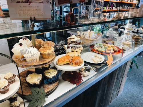 A display case filled with various baked goods, including cupcakes, pastries, and macarons, decorated with autumn leaves.