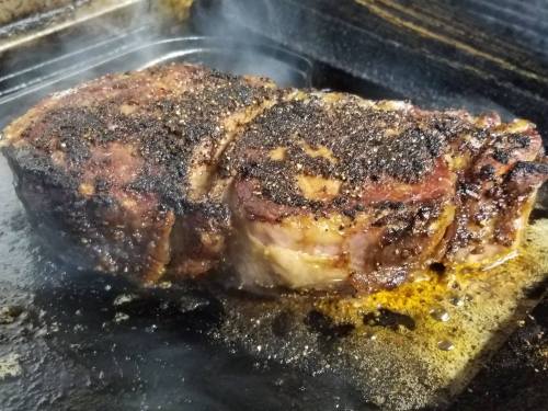 A perfectly cooked, charred piece of meat sizzling in a pan, surrounded by steam and juices.