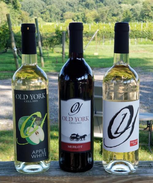 Three bottles of Old York Cellars wine: Apple White, Merlot, and a third white wine, set against a vineyard backdrop.
