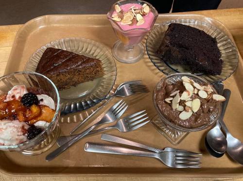 A tray with three desserts: chocolate cake, a pink parfait, and a fruit sundae, all garnished with almonds and spoons.