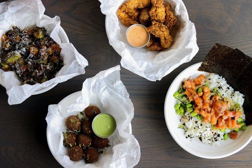 A variety of dishes on a table, including fried chicken, sushi, falafel, and Brussels sprouts with sauces.