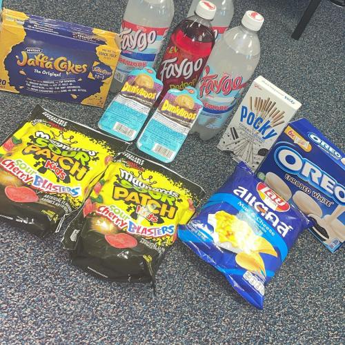 A variety of snacks and drinks including cakes, chips, soda, and candy arranged on a blue carpet.