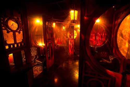 Dimly lit room with red hues, ornate doors, and vintage furniture, creating a mysterious and atmospheric ambiance.