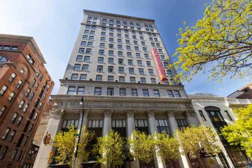 A tall historic building with a clear blue sky, surrounded by trees and urban architecture.