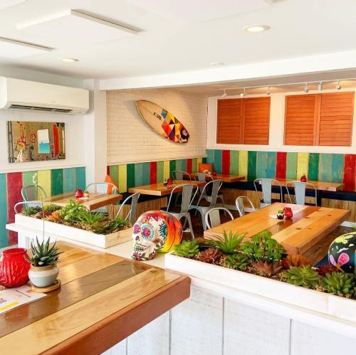 Brightly colored restaurant interior with wooden tables, surfboard decor, and vibrant wall art. Succulents add greenery.