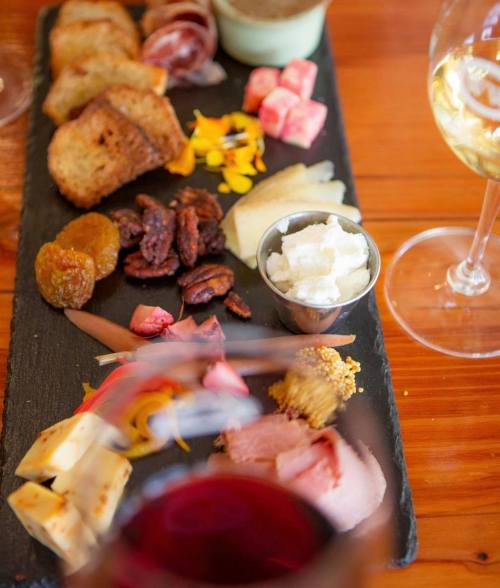 A charcuterie board with various meats, cheeses, nuts, and fruits, accompanied by glasses of white and red wine.