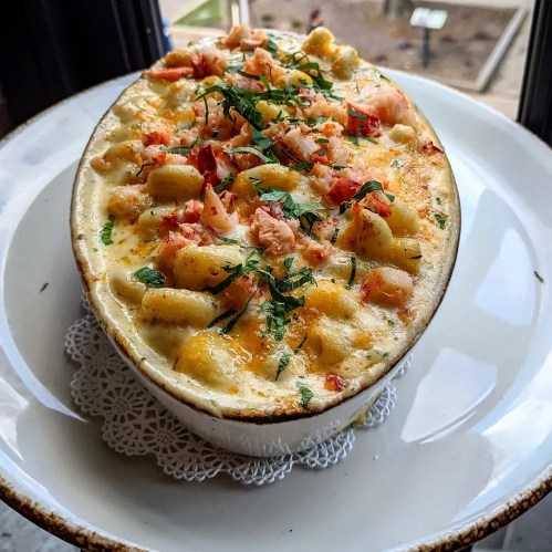 A creamy baked pasta dish topped with shrimp, herbs, and a golden crust, served in a white dish on a lace doily.