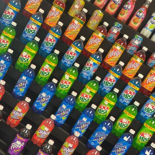 A colorful display of various soda bottles arranged on a shelf, featuring brands like Faygo and Hawaiian Punch.