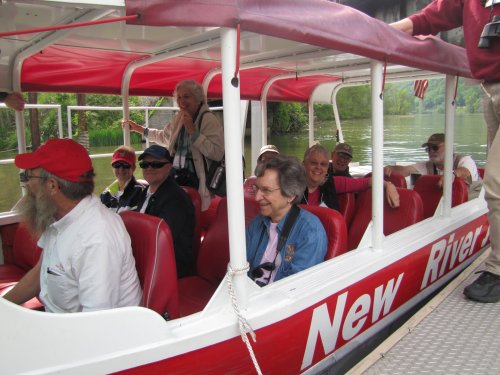 A group of people smiling and sitting inside a boat with red seats, enjoying a scenic river view.