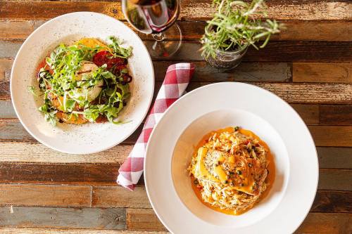 A plate of pasta with sauce and cheese, alongside a salad and a glass of red wine on a rustic wooden table.