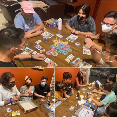 A group of people playing board games at a table, enjoying a fun and social atmosphere. Masks are worn by some.