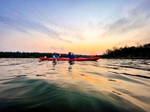 Two people in a red kayak on calm water at sunset, with a colorful sky and trees in the background.