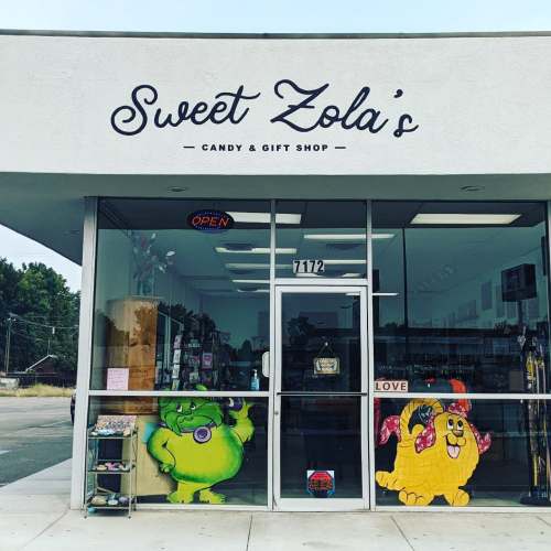 Exterior of Sweet Zola's Candy & Gift Shop, featuring colorful cartoon characters on the windows and an "Open" sign.