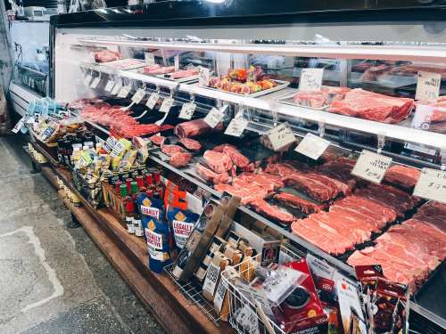 A meat display case filled with various cuts of beef, sausages, and condiments in a grocery store.