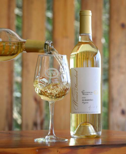 A bottle of Albariño wine being poured into a glass, with a wooden background.