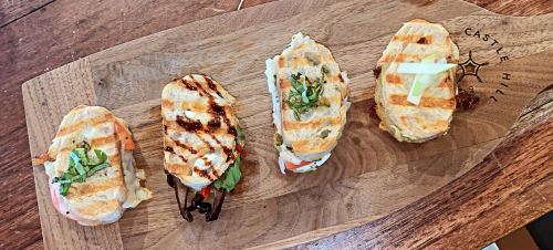 Four grilled sandwiches on a wooden board, garnished with herbs, showcasing a variety of fillings.