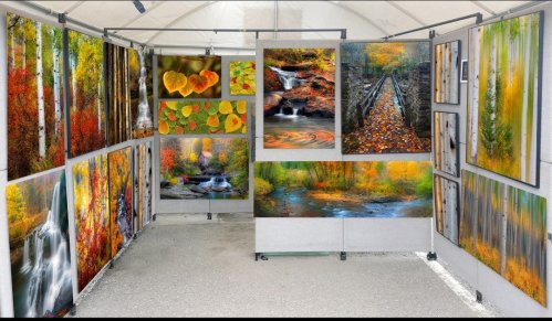Art gallery display featuring vibrant autumn landscapes and waterfalls on canvas, arranged in a tent.