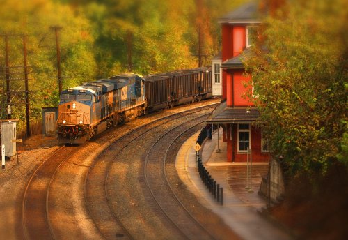 A train curves around a bend near a red station, surrounded by trees in autumn colors.
