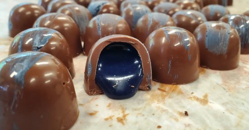 A close-up of chocolate candies, one with a blue filling oozing out, surrounded by others on a surface.