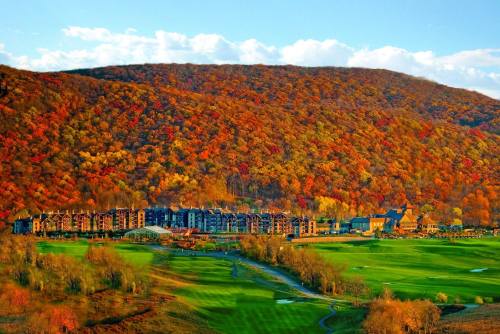 A scenic view of a resort nestled at the base of a colorful, autumn foliage-covered mountain.