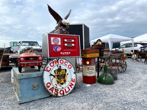 A collection of vintage gas station memorabilia and antiques displayed outdoors, including signs and a toy car.