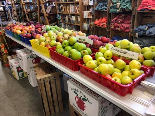 A display of various apple varieties in baskets, with labels for Mutzu and Golden Delicious, in a rustic store setting.
