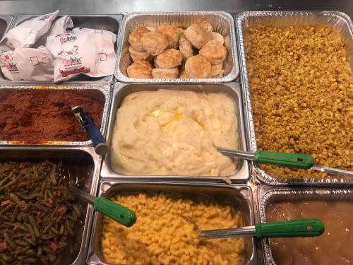 A buffet spread featuring biscuits, macaroni and cheese, mashed potatoes, green beans, and popcorn, with serving utensils.