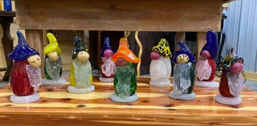 A collection of colorful glass gnome figurines arranged on a wooden surface.