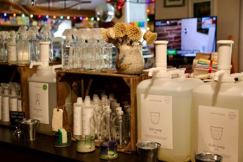 A cozy shop display featuring bottles of water, dish soap, and decorative items on wooden shelves.