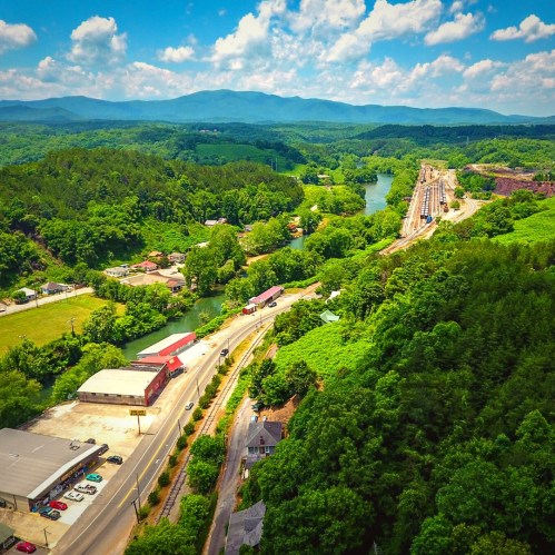 Aerial view of a lush green landscape with a river, mountains, and a small town along a winding road.