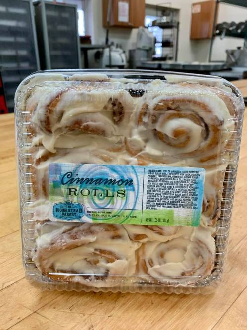 A clear plastic container holding cinnamon rolls with cream cheese frosting, labeled "Cinnamon Rolls."