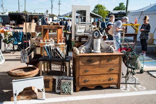 A bustling outdoor market featuring various vintage furniture and decor items for sale.