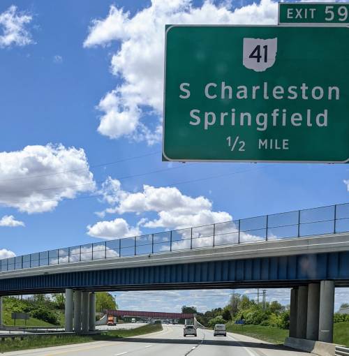Green highway sign for exit 41, S Charleston/Springfield, ½ mile ahead, with a blue sky and clouds in the background.