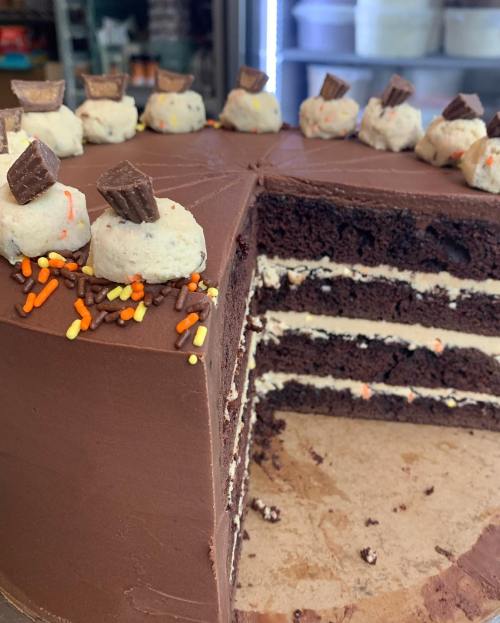 A chocolate cake with layers, topped with cookie dough balls and chocolate pieces, decorated with colorful sprinkles.