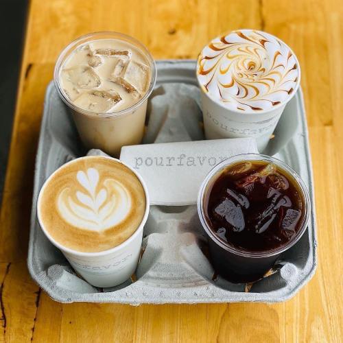 Four coffee drinks in cups on a wooden table, including iced coffee, a latte, and a decorative whipped cream topping.