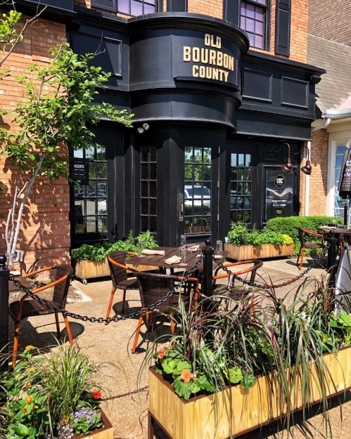 Exterior of a restaurant named "Old Bourbon County," featuring outdoor seating and vibrant planters.