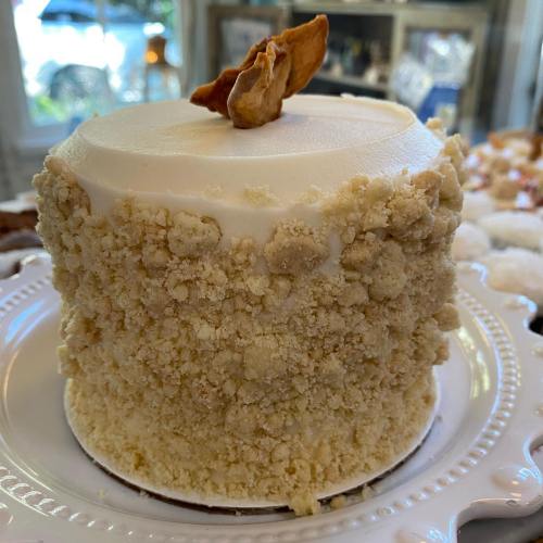 A small, round cake with a crumbly beige exterior and a smooth white frosting on top, garnished with a nut.