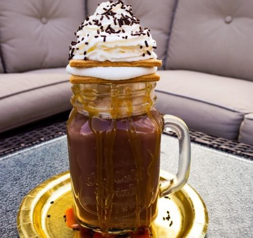 A mason jar filled with chocolate drink, topped with whipped cream, sprinkles, and a cookie, sitting on a gold plate.