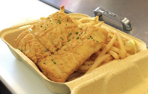 A takeout container with two pieces of fried fish and a side of golden French fries, garnished with green herbs.