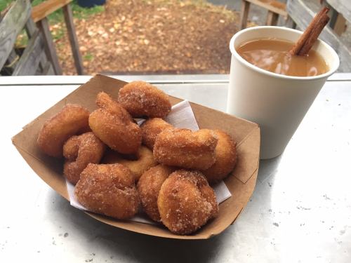 A tray of golden-brown doughnuts dusted with sugar next to a cup of coffee with a cinnamon stick.