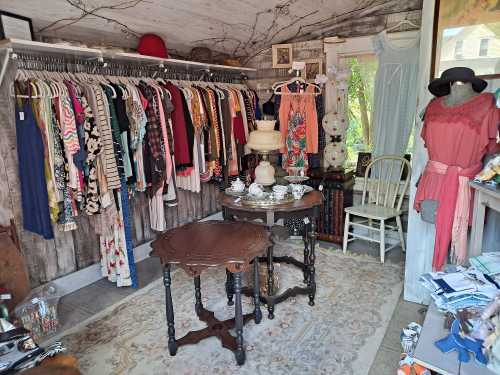 A cozy vintage shop interior with colorful clothing racks, a table set with tea, and various decor items.