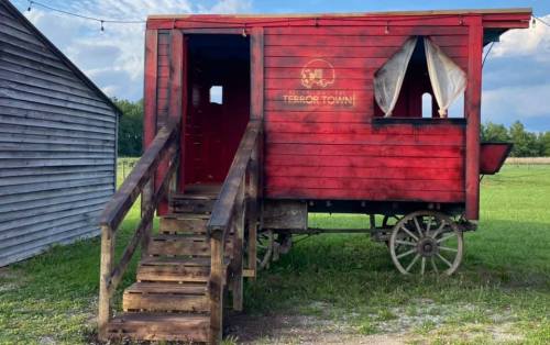 A red wooden wagon with a staircase, set in a grassy area, featuring a window and a logo on the side.