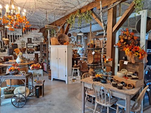 A cozy shop filled with rustic decor, vintage items, and autumn-themed arrangements, featuring wooden furniture and warm lighting.
