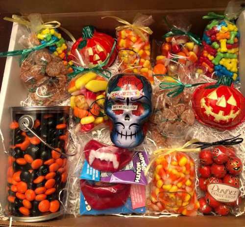 A festive assortment of Halloween candies, including jars, bags, and a decorative skull, arranged in a box.