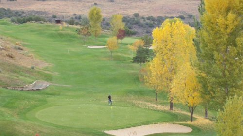 A golfer on a green surrounded by trees with autumn foliage on a scenic golf course.