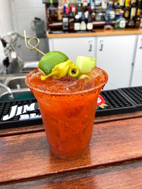 A vibrant Bloody Mary in a glass, garnished with lime, celery, and olives, on a wooden bar top.